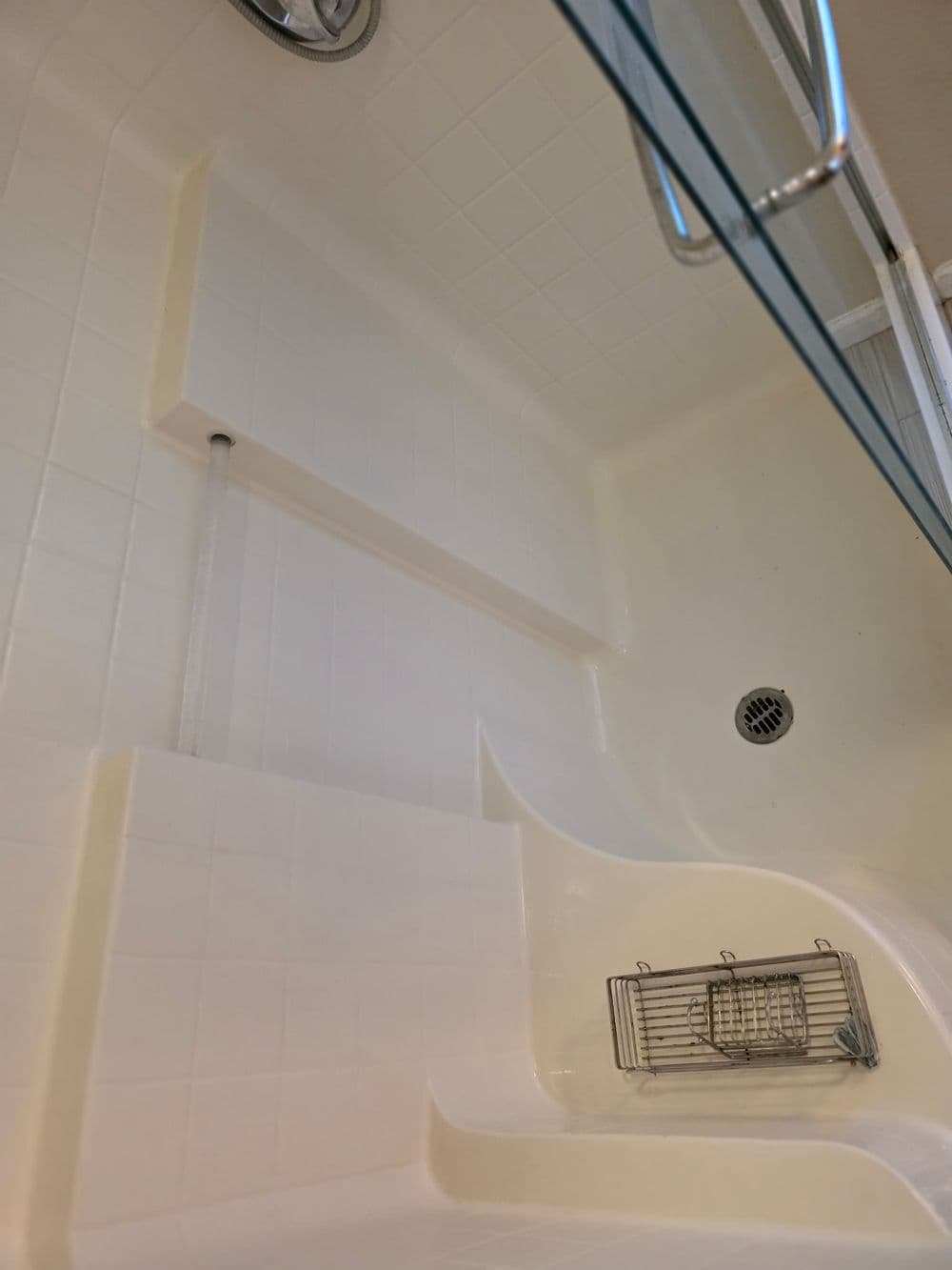 Clean, modern shower interior with built-in seating and stainless steel storage rack.