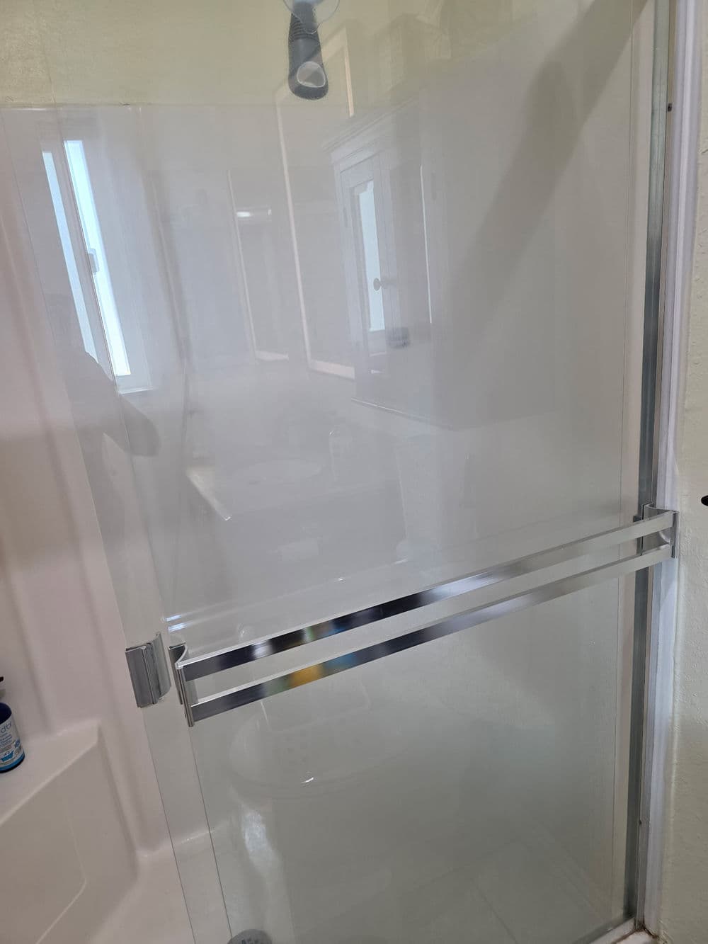 Transparent glass shower door with chrome handles in a well-lit bathroom setting.